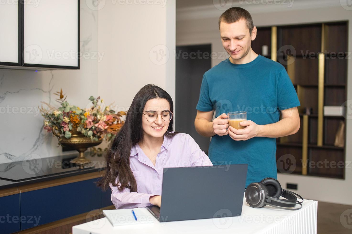 un' ragazza con bicchieri è guardare a un' computer portatile, un' uomo è in piedi Il prossimo per sua e potabile caffè foto