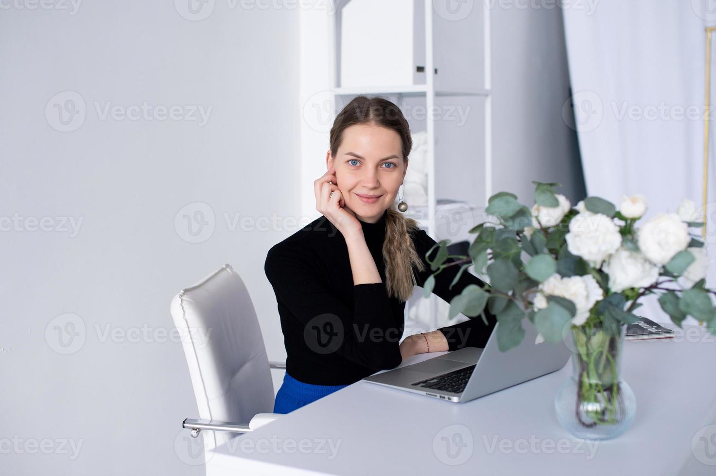 il ragazza lavori nel un' bianca ufficio con un' il computer portatile e fiori su il tavolo foto