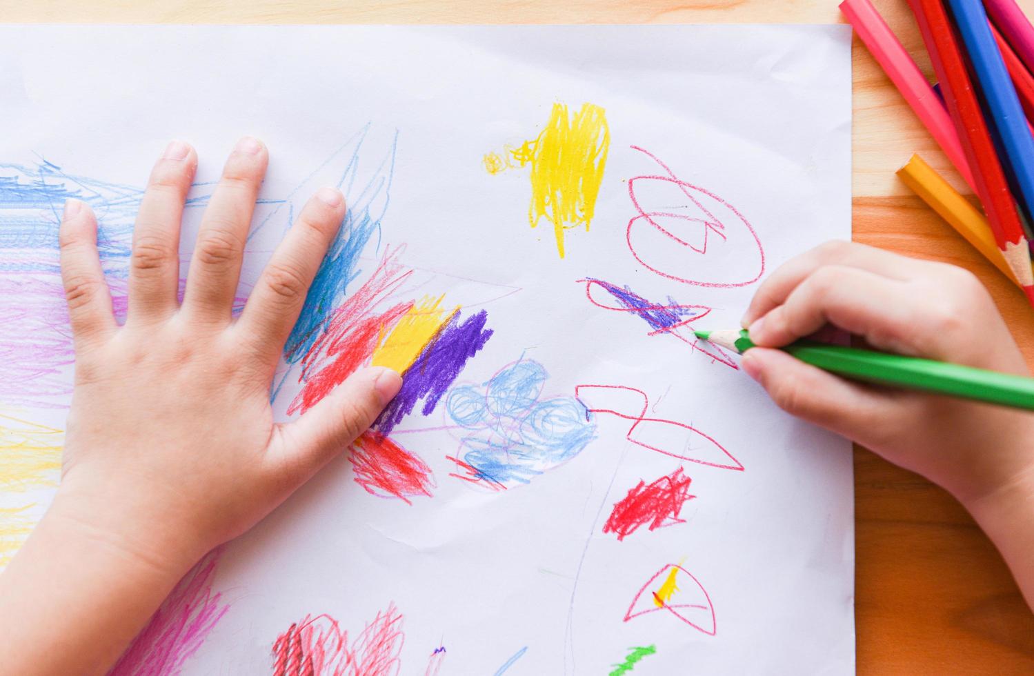 ragazza che dipinge su un foglio di carta con matite colorate sul tavolo di legno a casa - bambino che fa un disegno e pastello colorato foto
