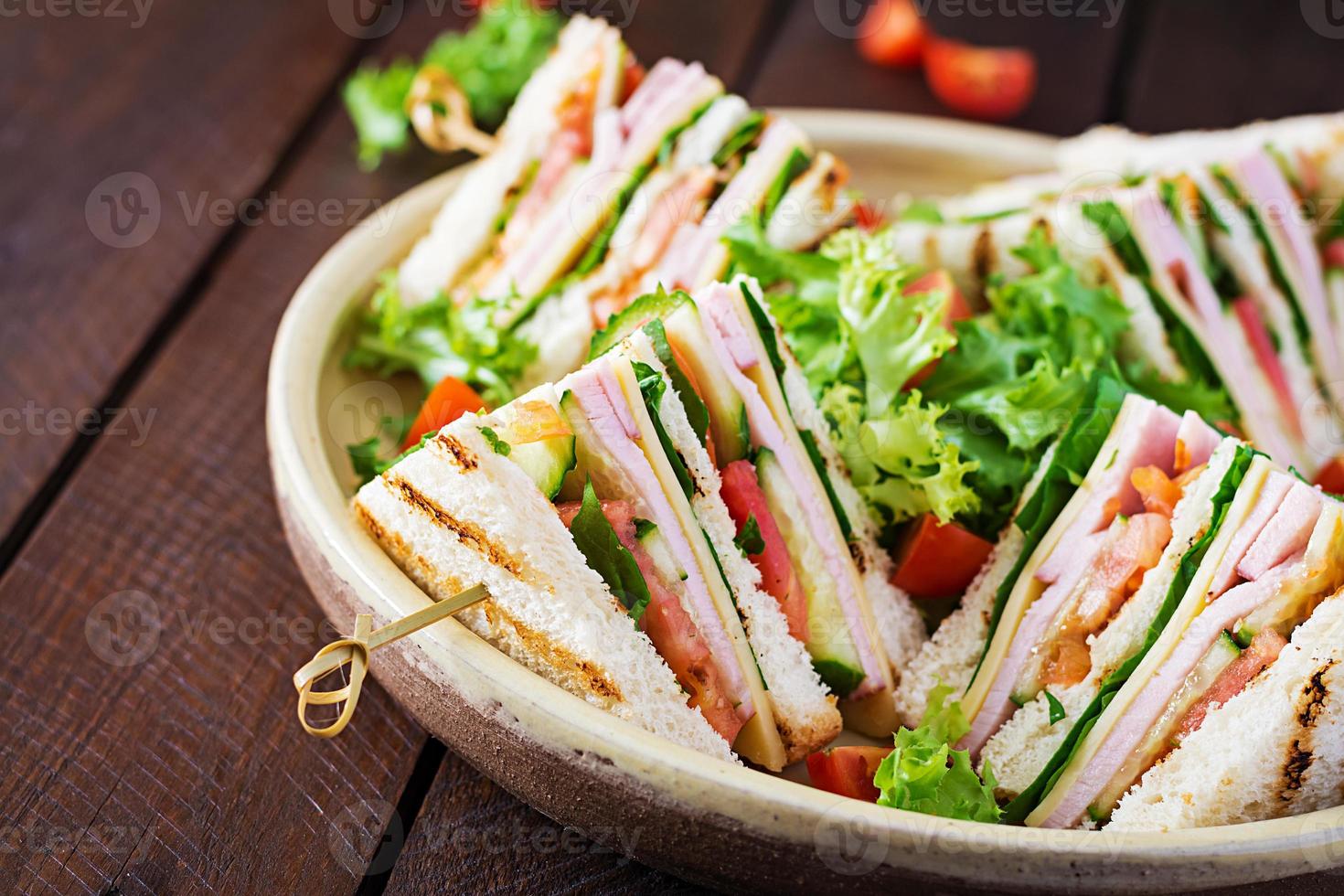 club Sandwich con prosciutto, pomodoro, cetriolo, formaggio, e rucola su di legno sfondo. foto