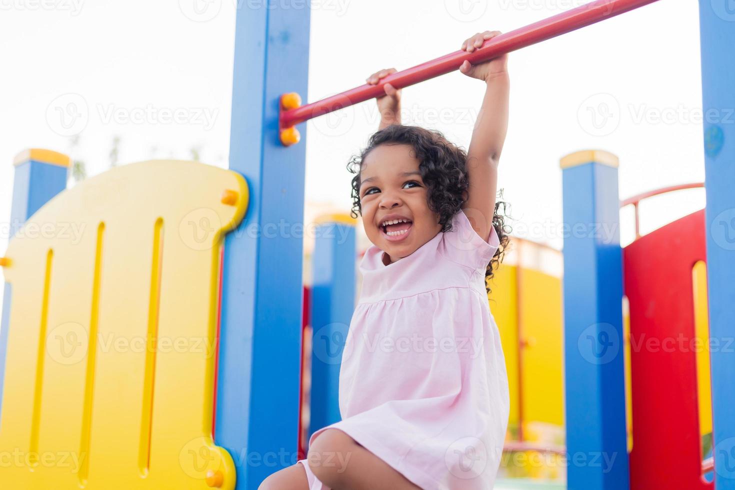 bruno bambino con Riccio capelli nel un' pallido rosa vestito giochi su un' strada terreno di gioco e cavalcate giù il collina. il concetto di un' salutare stile di vita. contento infanzia. alto qualità foto