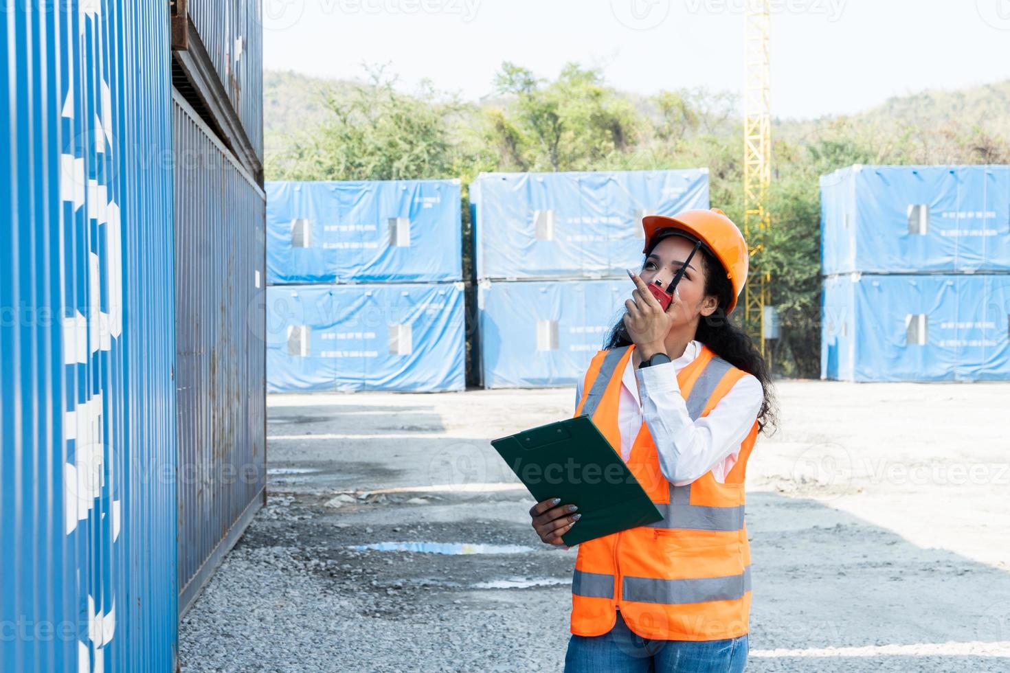 sorridente ritratto di bellissimo asiatico femmina industriale ingegnere indossare bianca casco, veste Tenere walkie talkie. sicurezza supervisore a contenitore terminale foto