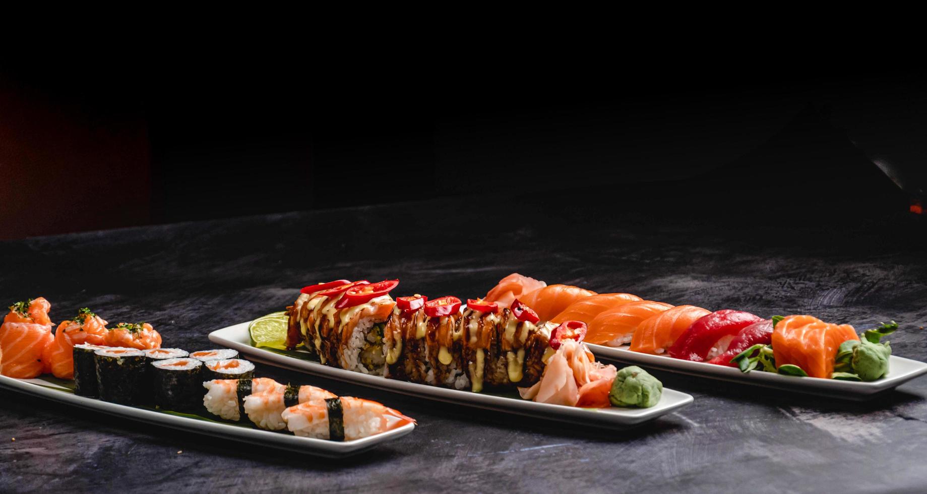 piatti pieno con diverso tipi di Sushi, Saki Sushi, kraken Sushi, salmone come Sushi, nigiri Sushi, e salmone Hosomaki Sushi su un' nero tavolo. foto