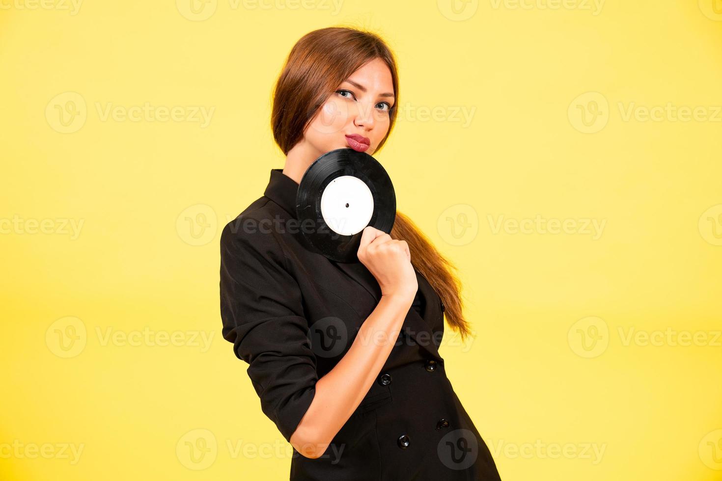 ragazza nel un' nero completo da uomo su un' giallo sfondo con un' disco nel sua mani, musica, il ragazza Spettacoli emozioni foto