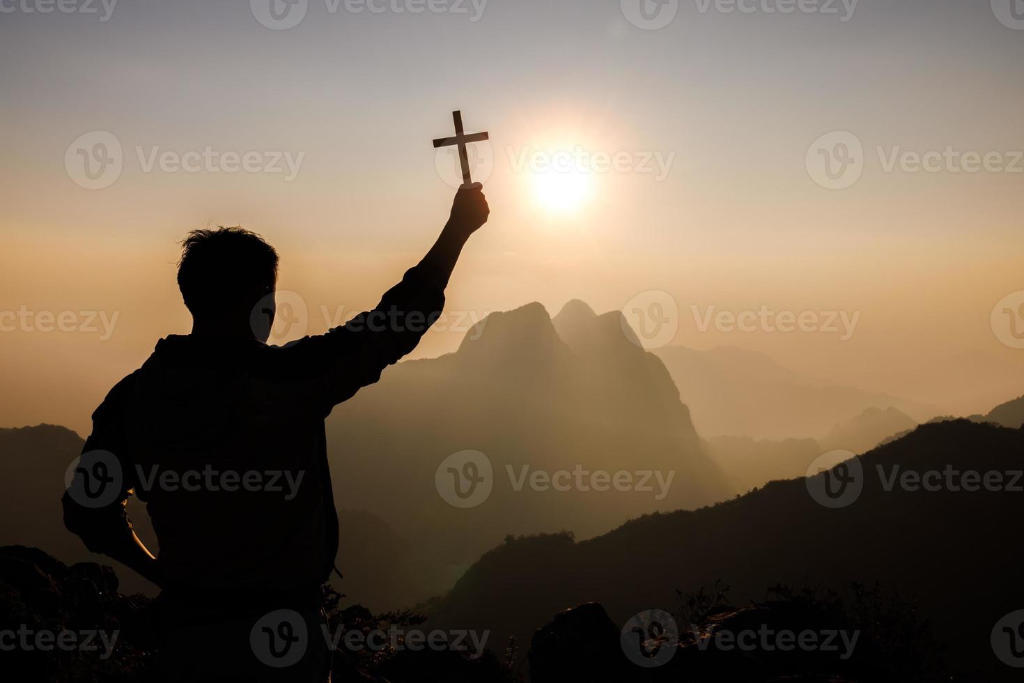 silhouette di giovane uomo preghiere e Tenere cristiano attraversare per adorazione Dio a tramonto sfondo. cristiano religione concetto sfondo. foto