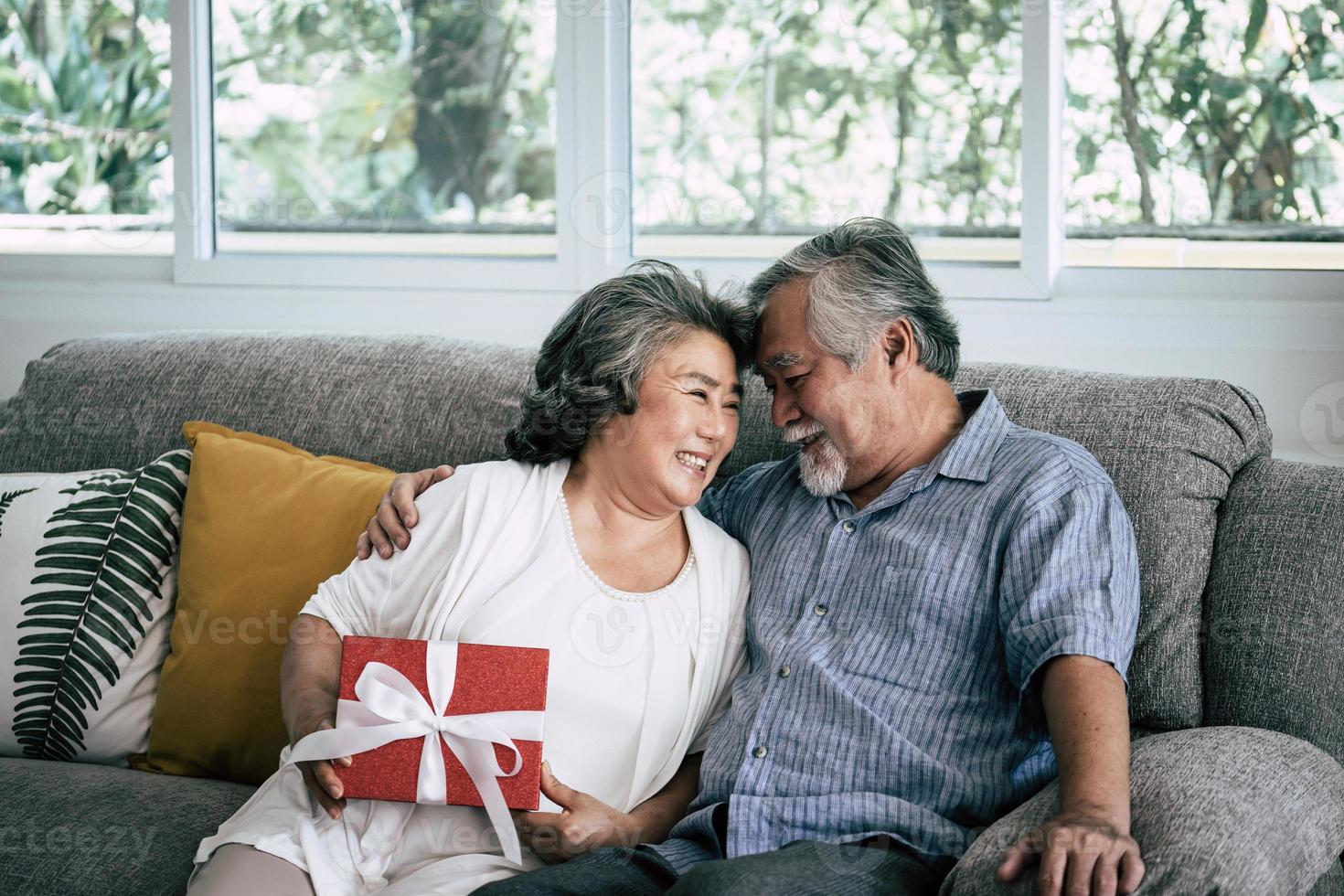 sorprese coppia di anziani con confezione regalo in soggiorno foto