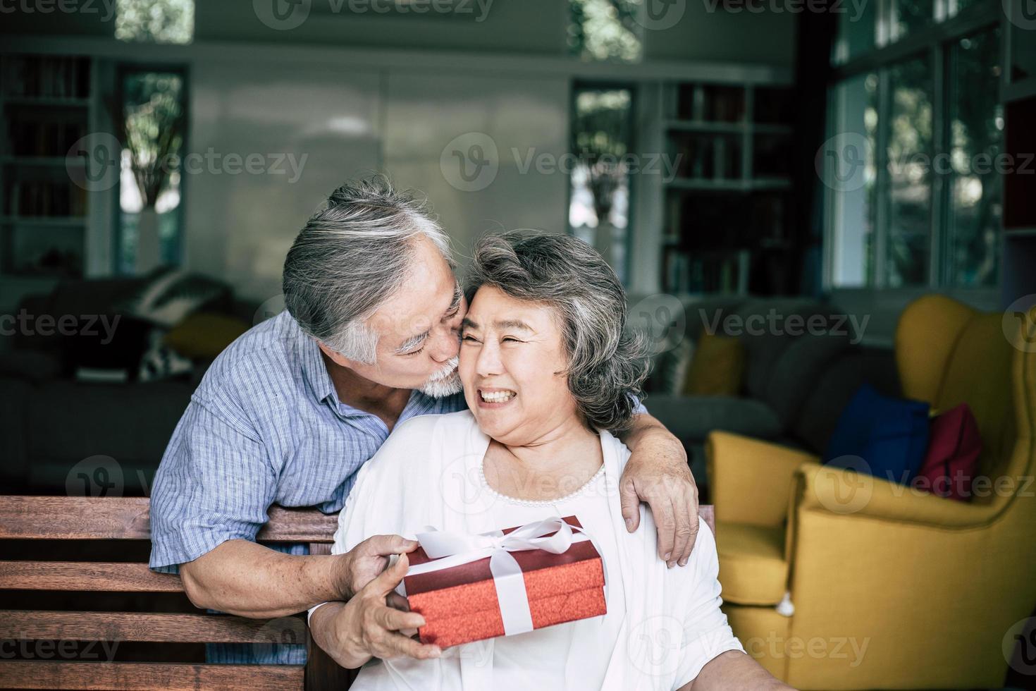 sorridente senior marito facendo sorpresa dando confezione regalo a sua moglie foto