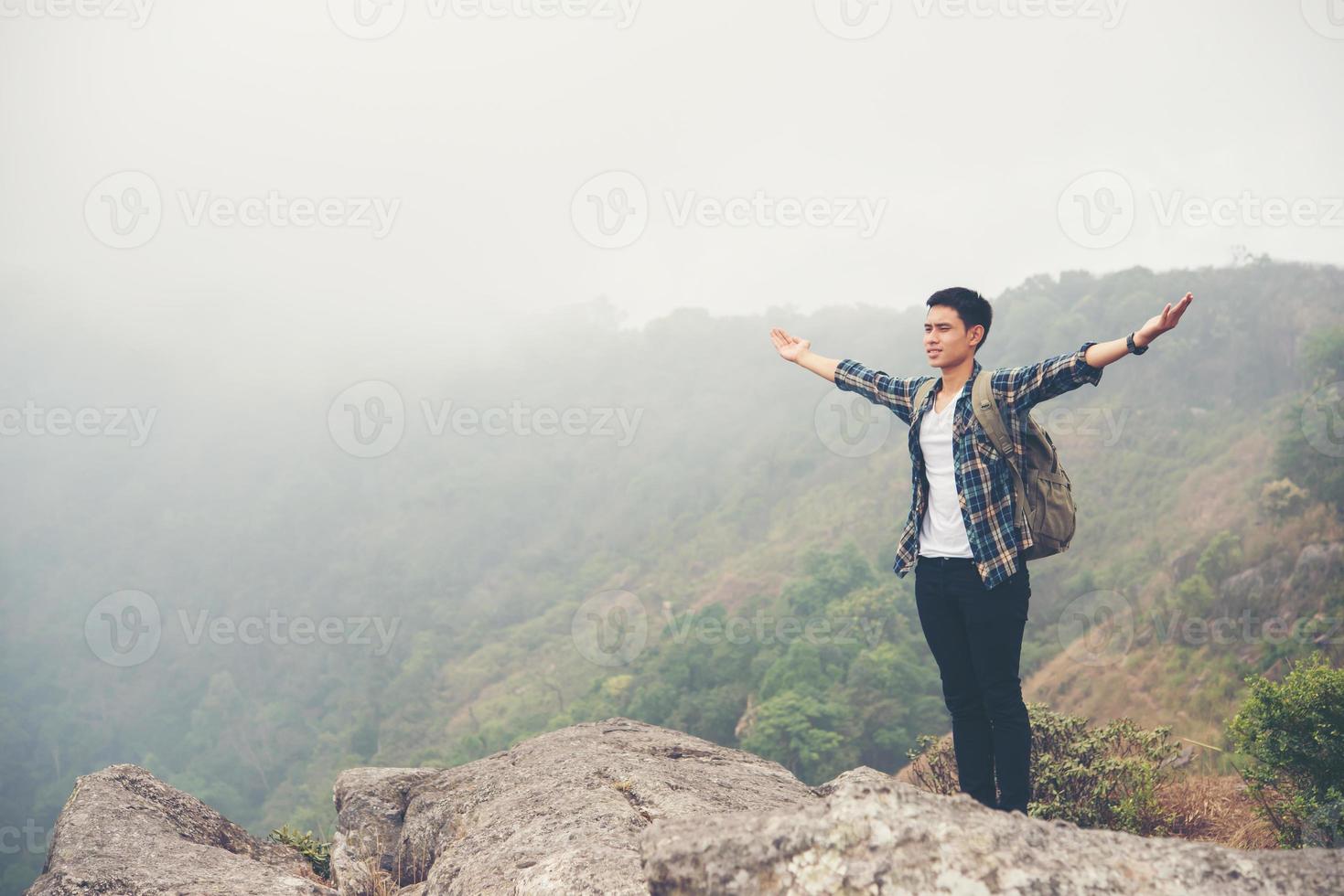 escursionista con zaino in piedi sulla cima di una montagna con le mani alzate foto