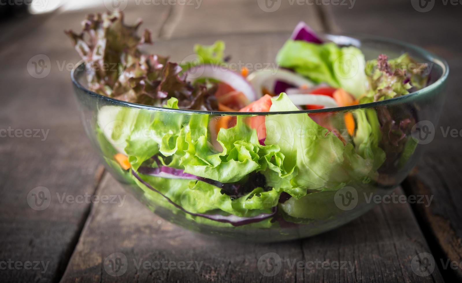 insalata di verdure fresche in una ciotola di vetro su fondo in legno foto