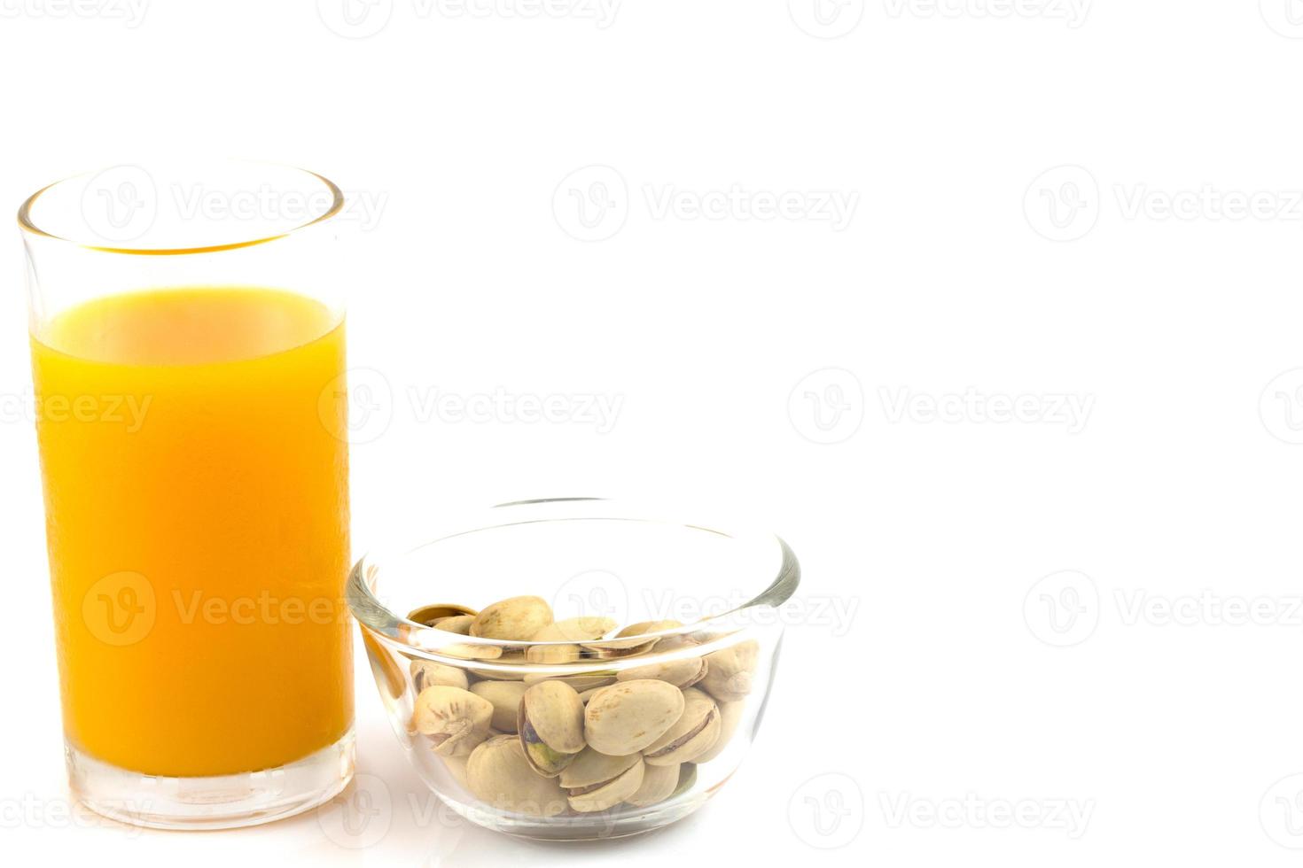 pistacchi in una lastra di vetro e un bicchiere di succo d'arancia isolato su bianco foto