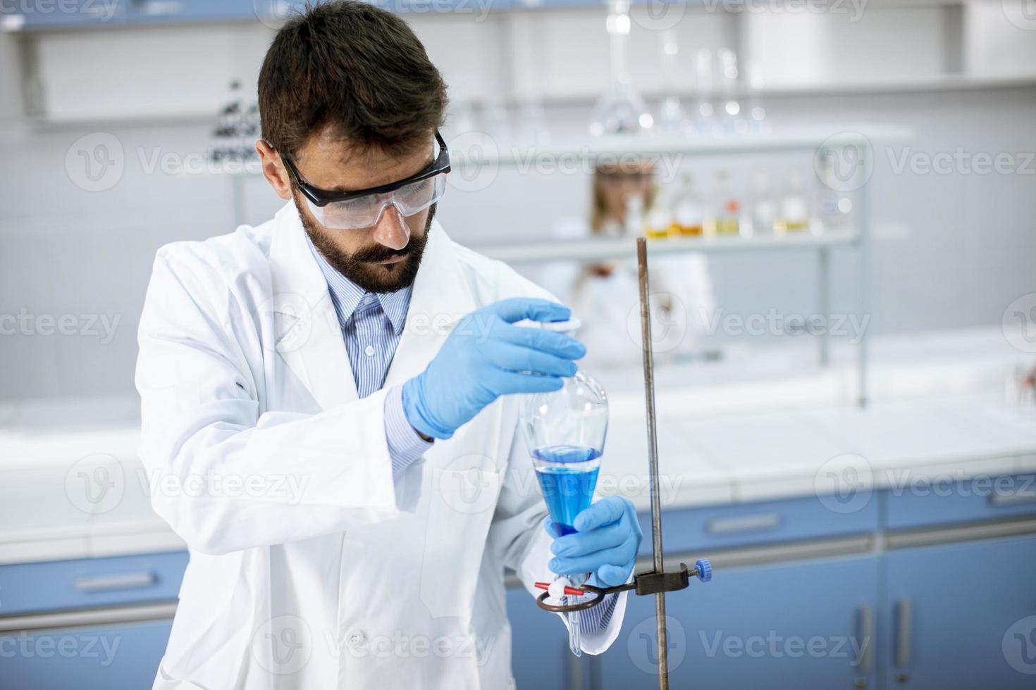 ricercatore che lavora con liquido blu al vetro del laboratorio foto