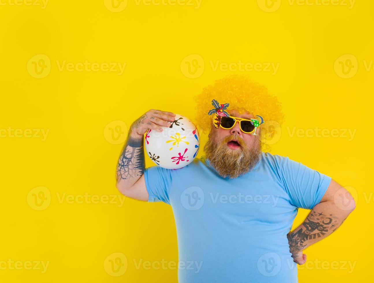 Grasso uomo con parrucca nel testa e occhiali da sole avere divertimento con un' palla foto