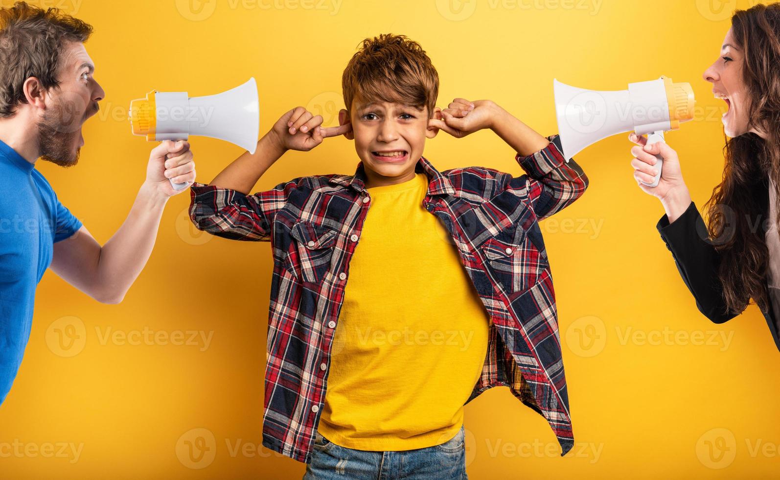 bambino coperture il suo orecchie perché lui fa non volere per sentire il grida e rimproveri di il suo genitori. giallo sfondo foto