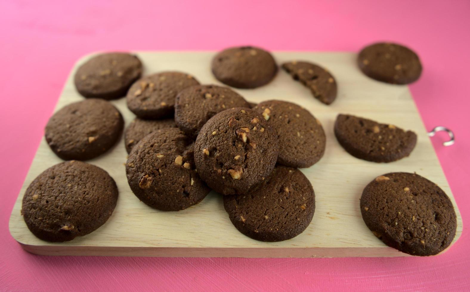 biscotti al cioccolato fondente al forno su un tagliere di legno su uno sfondo rosa foto