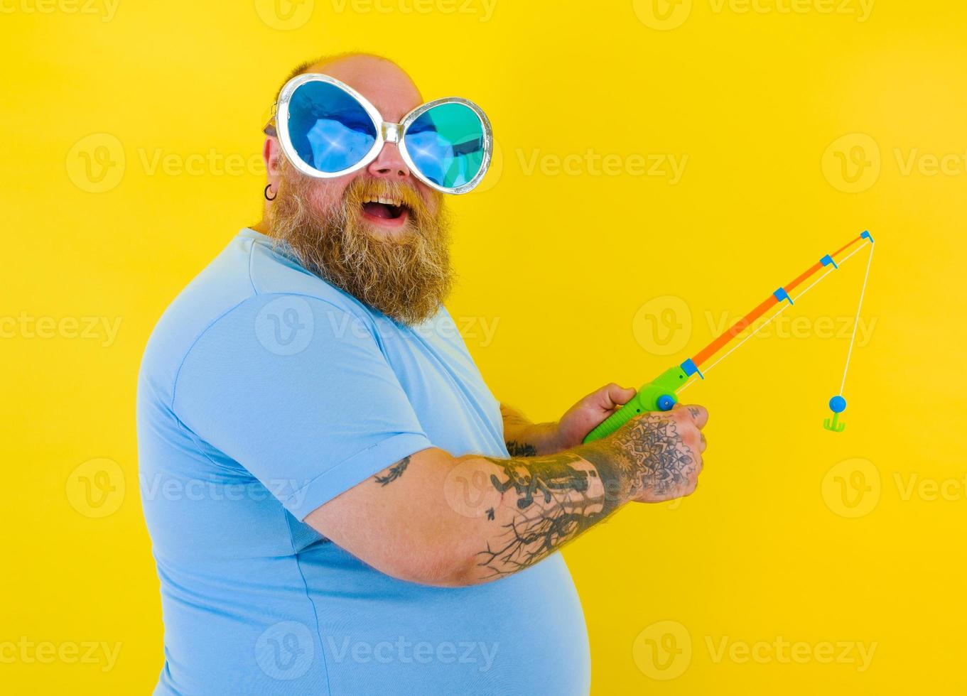 Grasso uomo con barba e occhiali da sole avere divertimento con il pesca asta foto