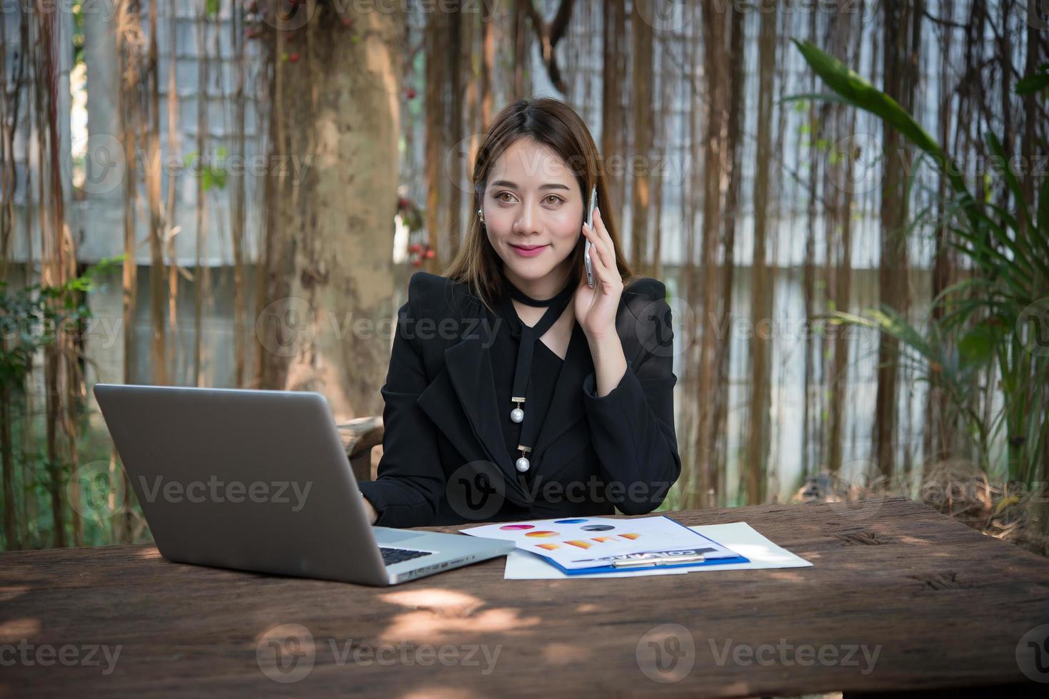 donna d'affari parlando al telefono e utilizzando il suo computer portatile seduto su un tavolo a casa foto