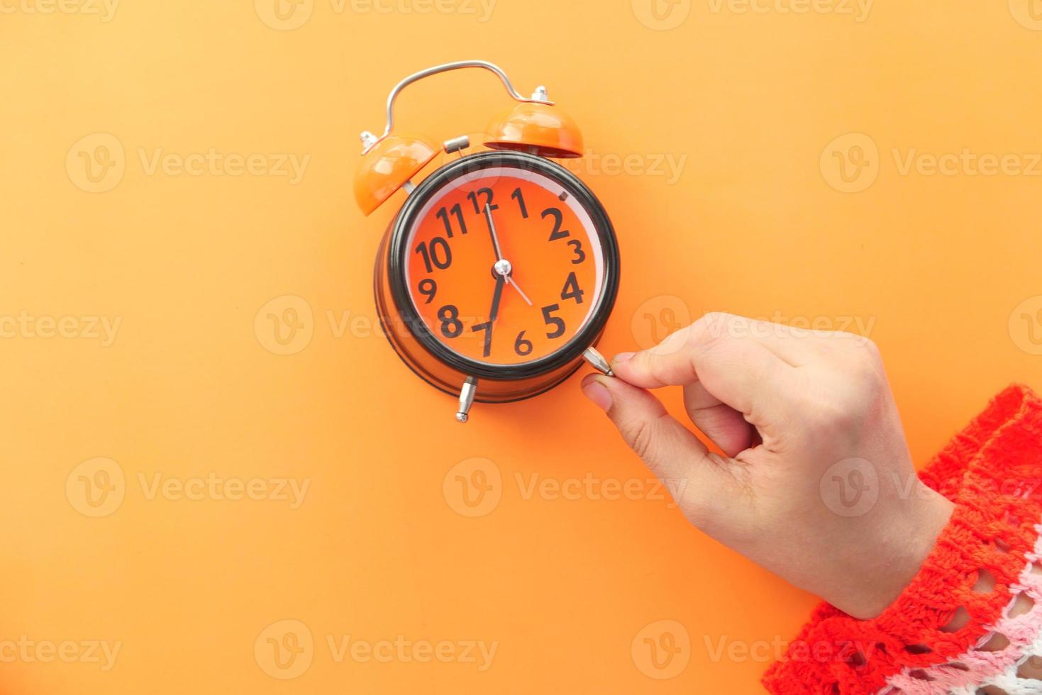 mano della donna che tiene sveglia su sfondo arancione foto