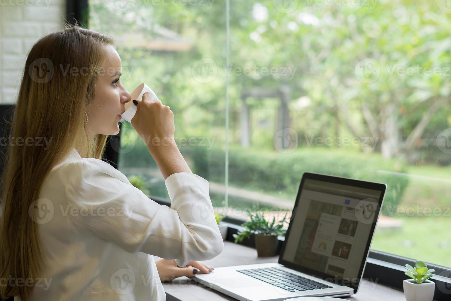 giovane donna d'affari di bere il caffè mentre si lavora sul suo computer portatile in ufficio foto