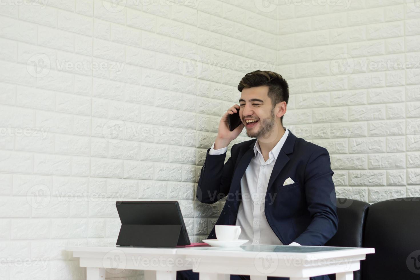 giovane imprenditore utilizza lo smartphone mentre si lavora sul suo laptop in ufficio foto