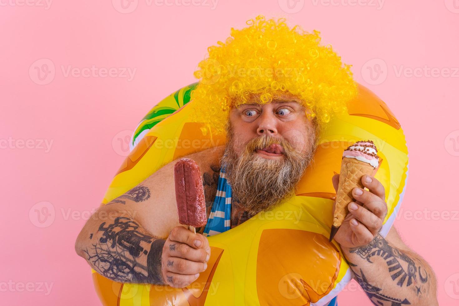 Grasso uomo con barba e parrucca mangia un' ghiacciolo e un gelato foto