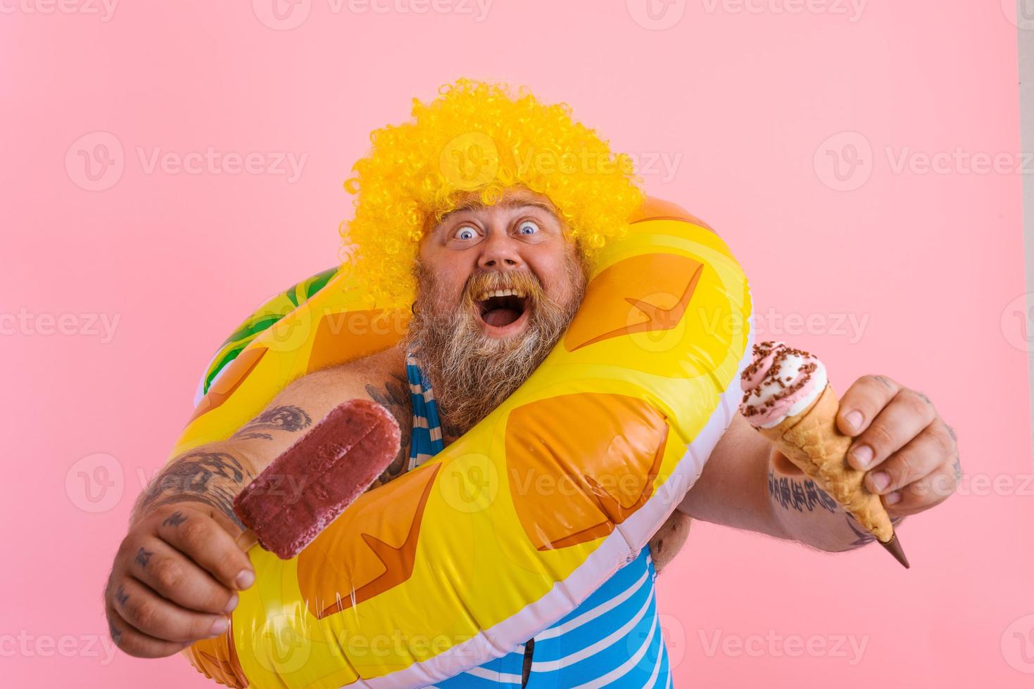 Grasso uomo con barba e parrucca mangia un' ghiacciolo e un gelato foto