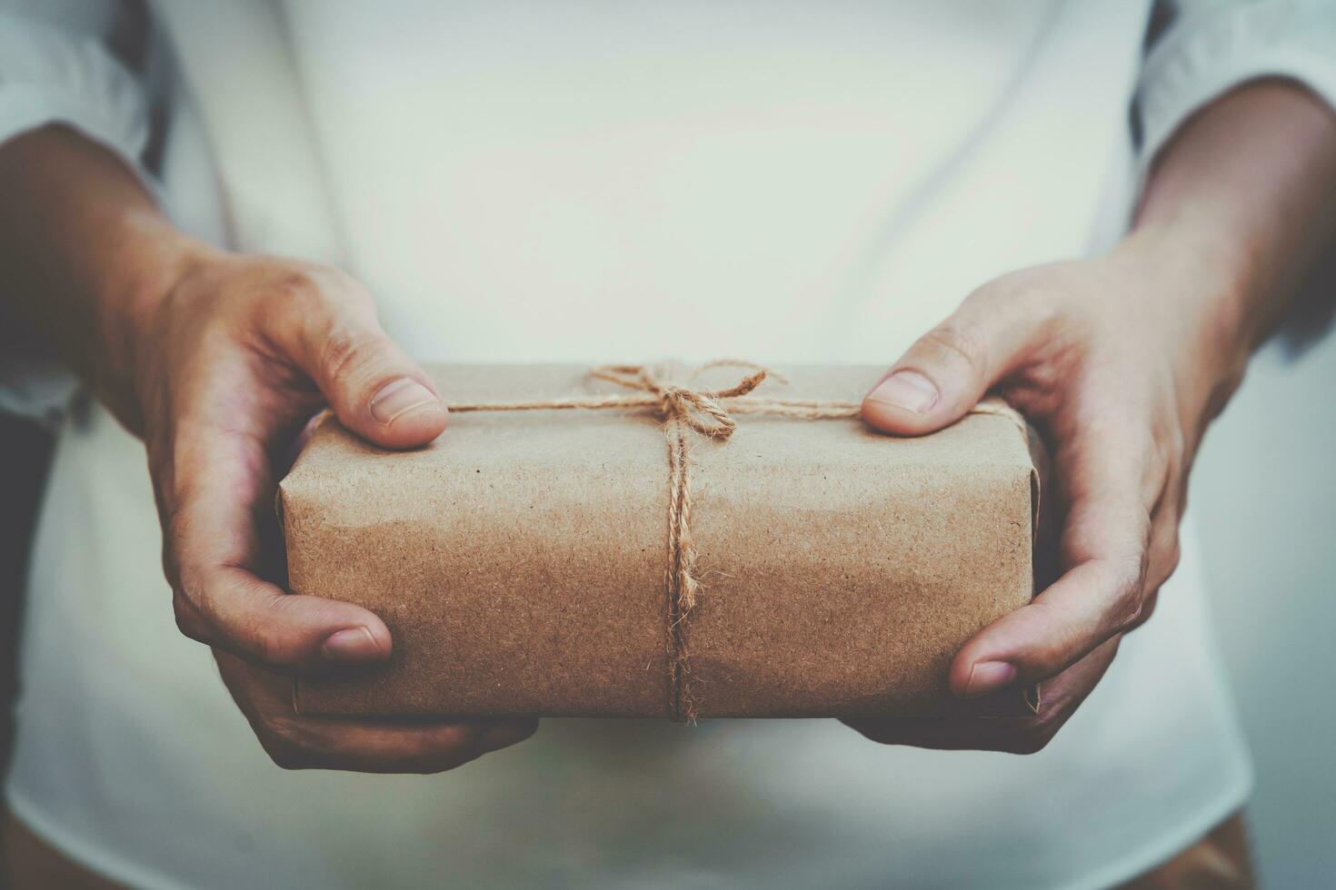 vicino su mano donna presente e Tenere kraft regalo scatola confezione. foto