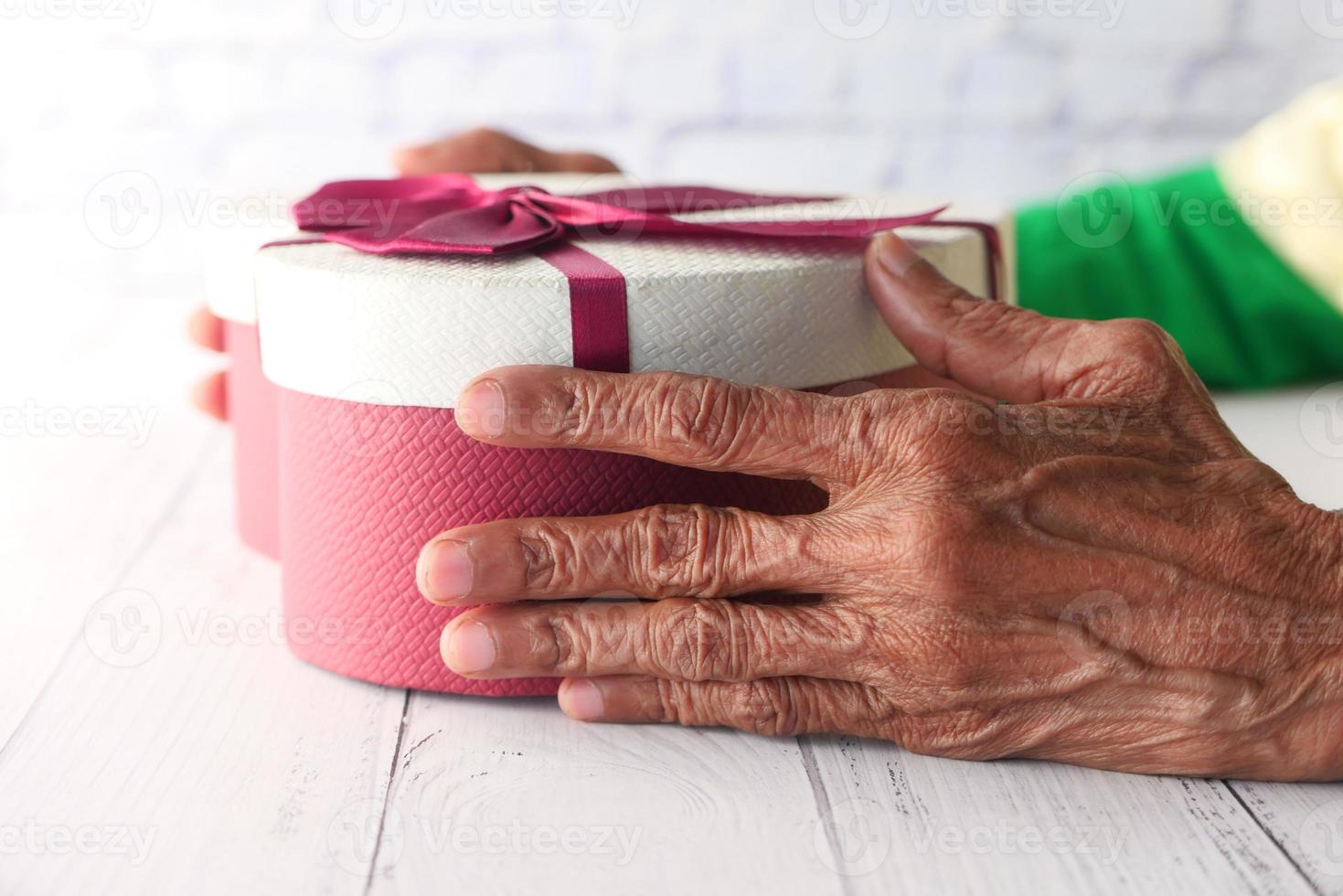 mani della donna anziana che tengono una scatola regalo a forma di cuore foto