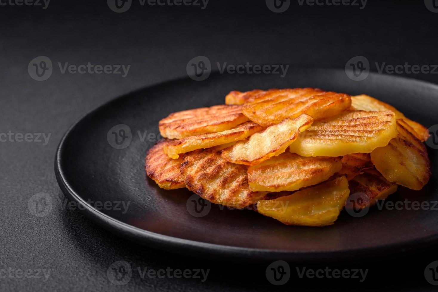 delizioso croccante fritte patate nel fette su un' nero ceramica piatto foto