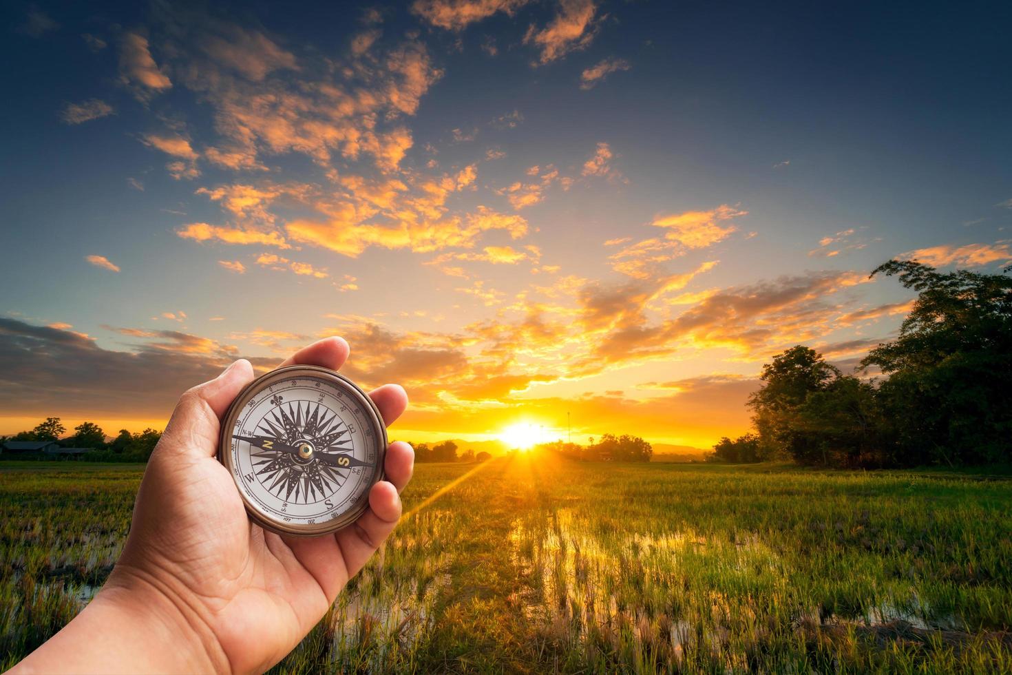 un' uomo Tenere bussola su mano a campo e tramonto per navigazione guida. foto