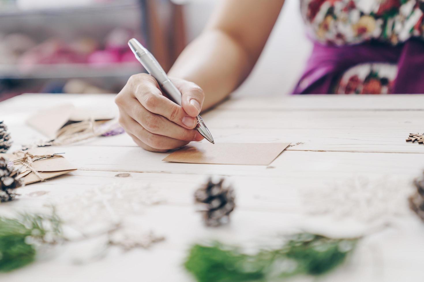 vicino su di mani donna scrittura vuoto Lista dei desideri e Natale carta su di legno tavolo con natale decorazione. foto