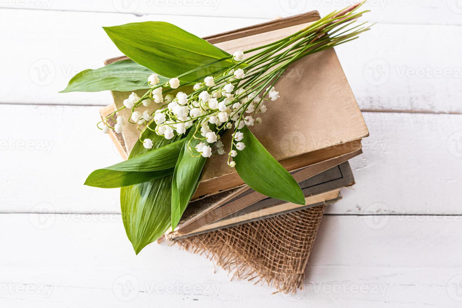 un' delicato mazzo di primavera gigli di il valle bugie su un' pila di vecchio libri, tela ruvida e un' di legno bianca tavolo. foto