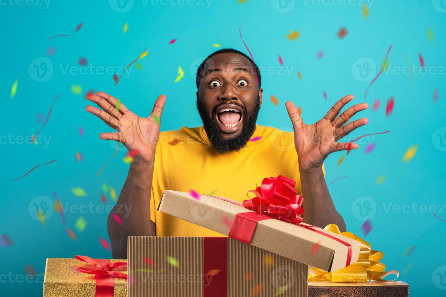 contento e stupito uomo si apre i regali su il suo compleanno. isolato su ciano sfondo foto