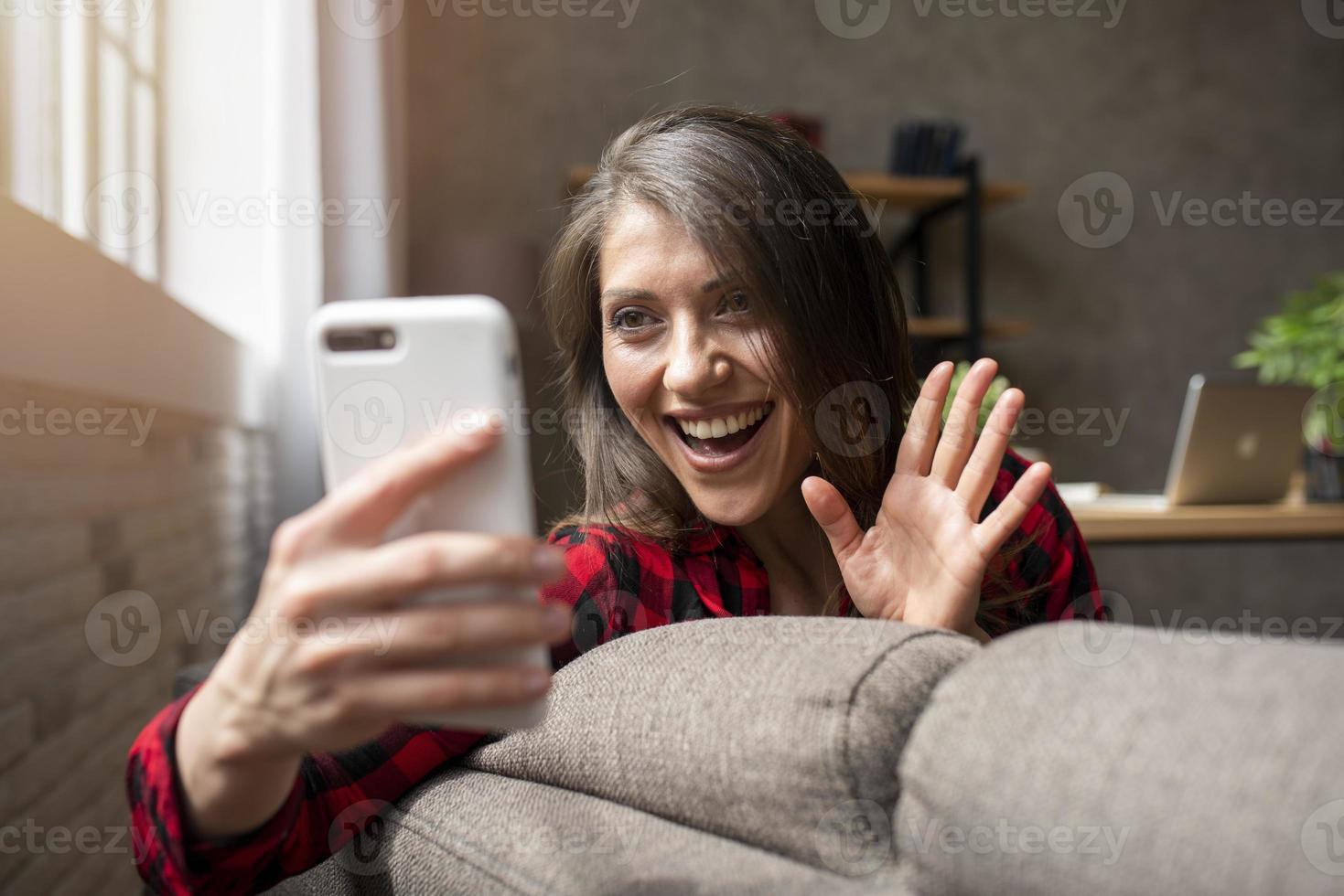 donna inizia un' video chiamata con sua smartphone su il divano foto