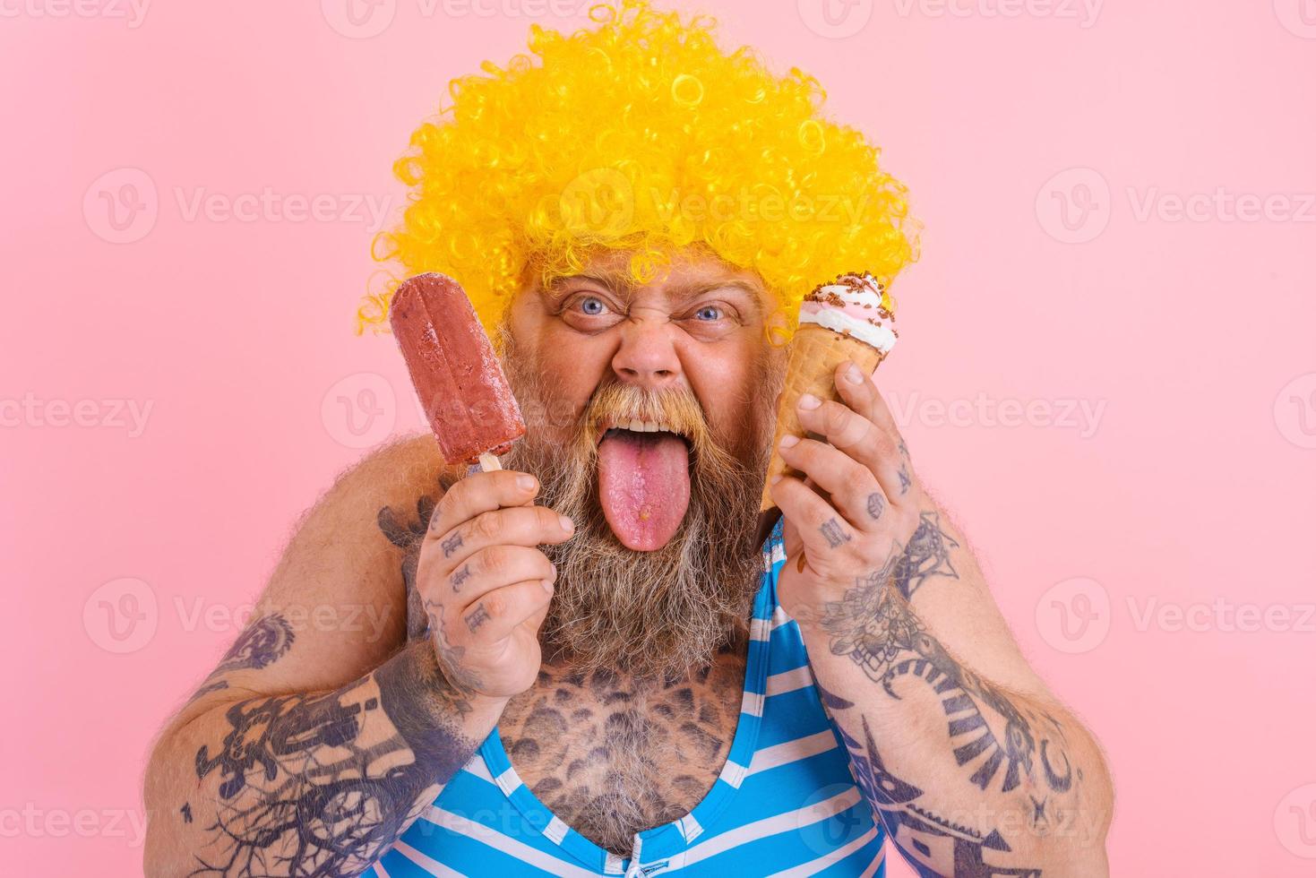 Grasso uomo con barba e parrucca mangia un' ghiacciolo e un gelato foto