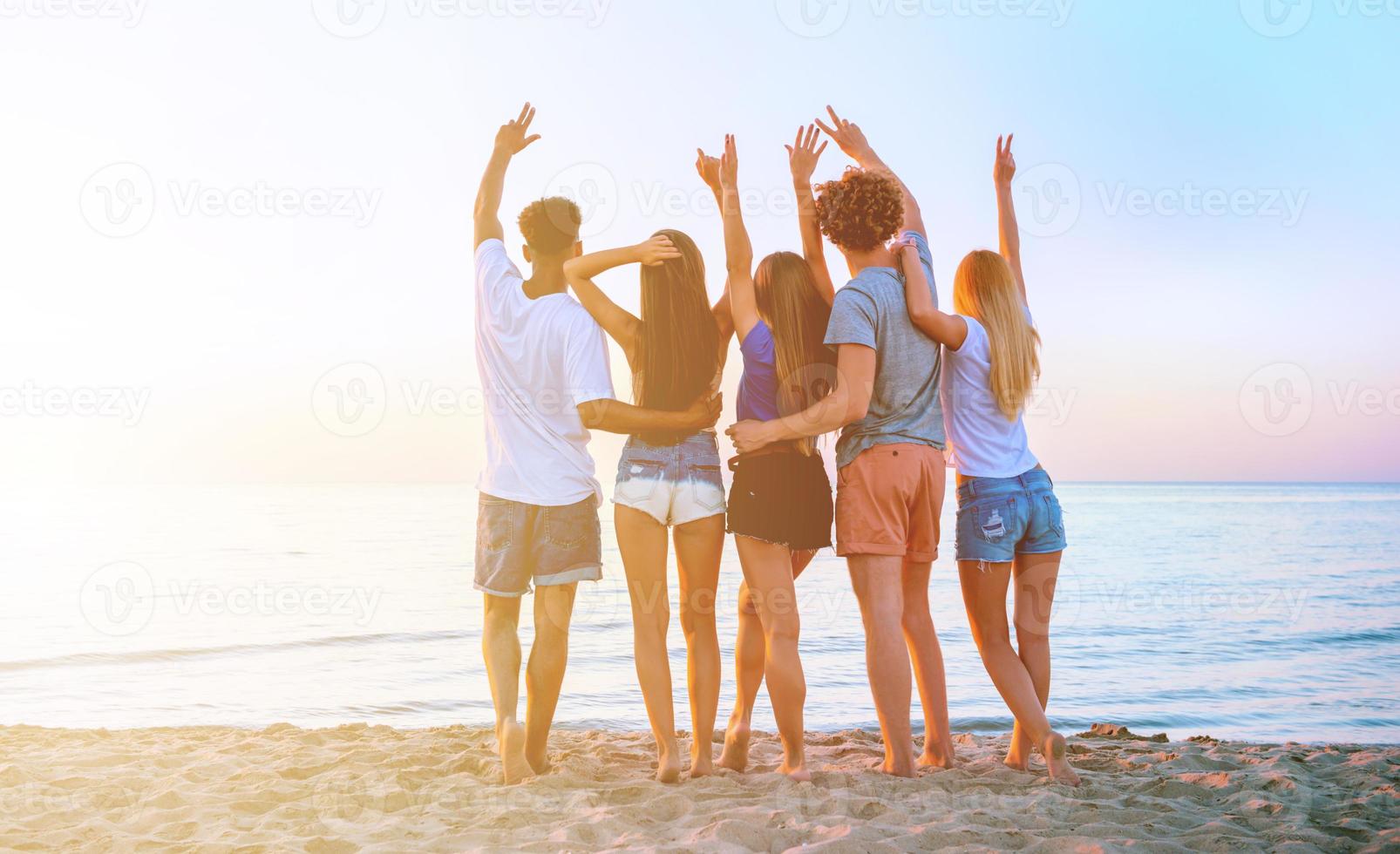 gruppo di contento amici avendo divertimento a oceano spiaggia a alba foto