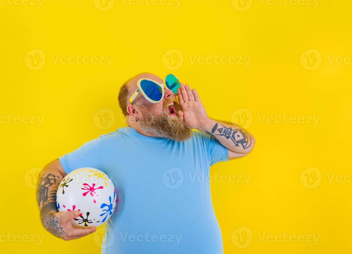 Grasso uomo con barba e occhiali da sole urla con un' palla nel mano foto