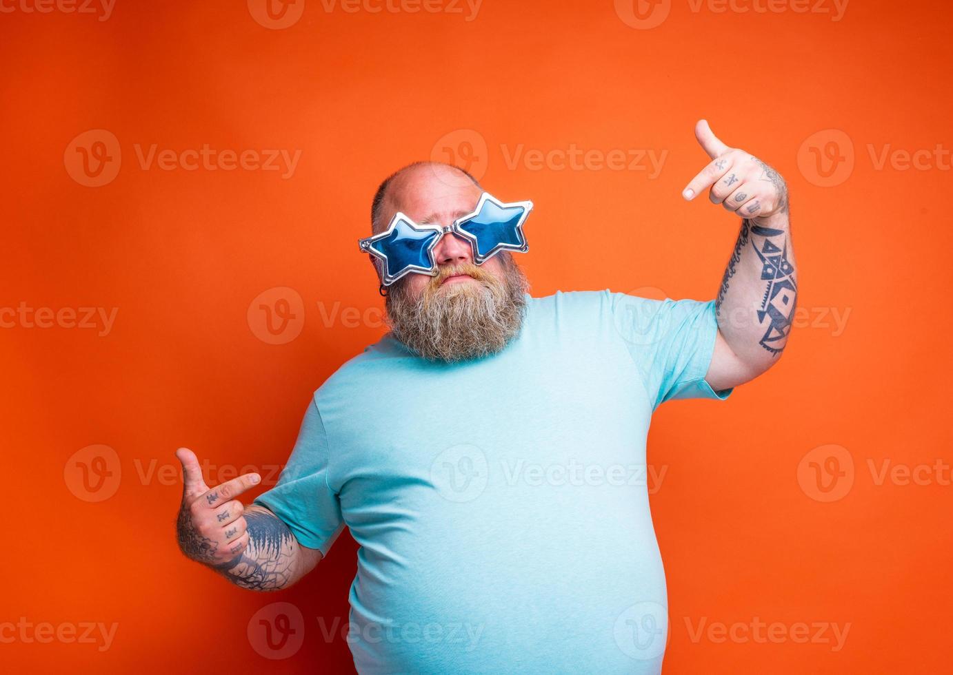 Grasso delusione uomo con barba, tatuaggi e occhiali da sole è incerto per qualcosa foto