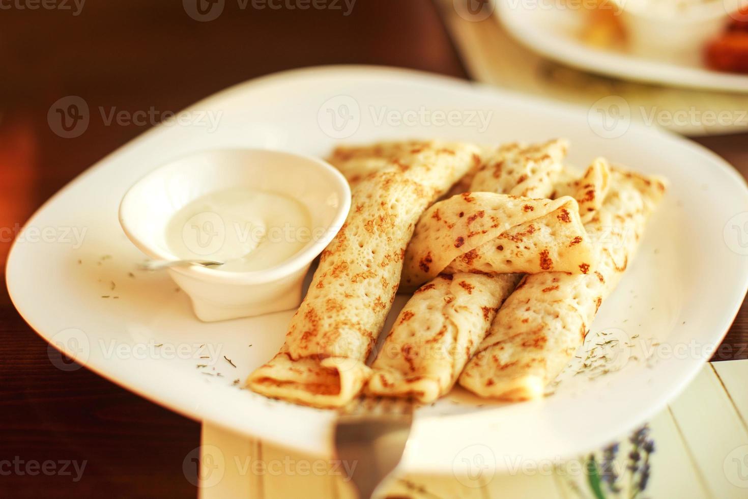 Pancakes lanciato nel un' cannuccia su un' piatto con acida crema foto