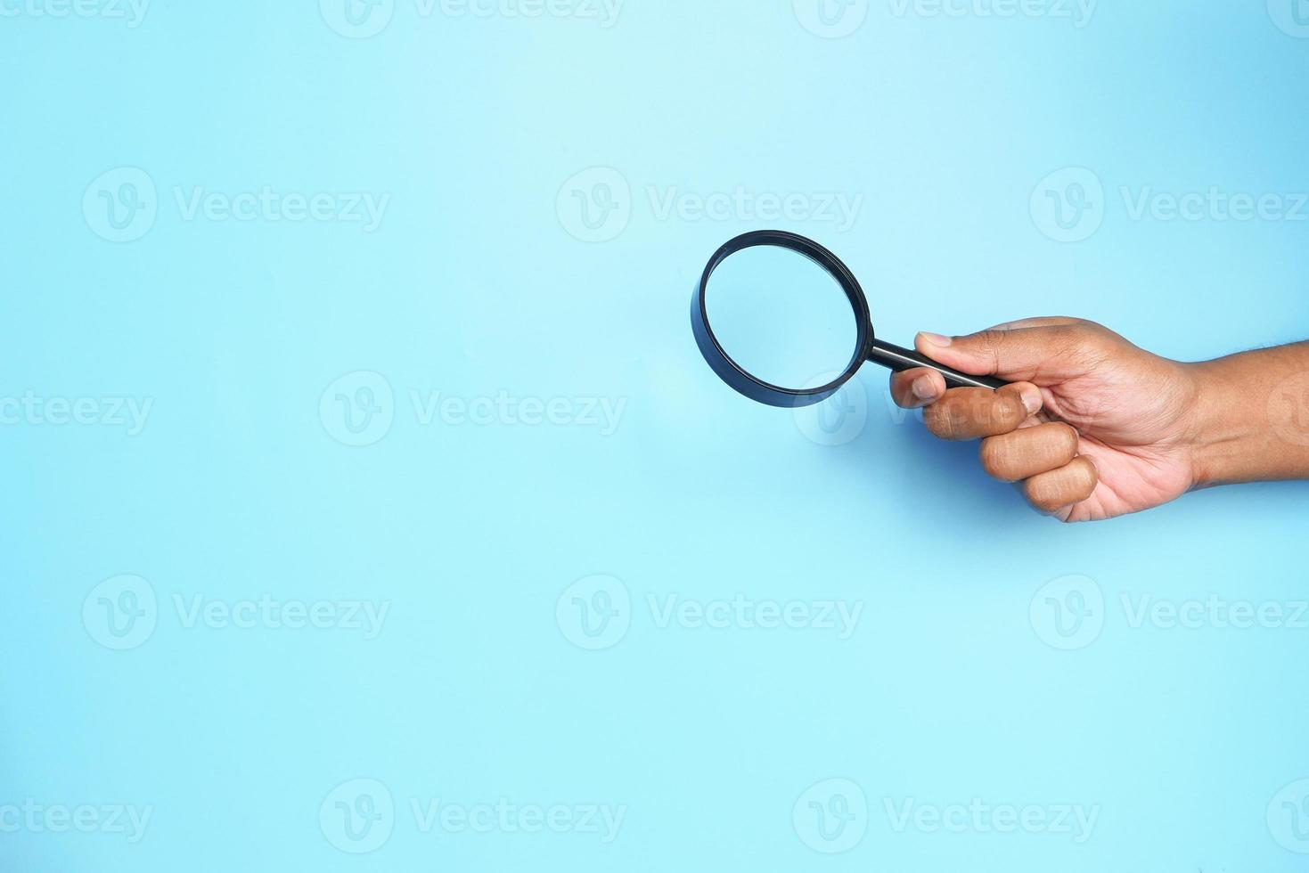 mano che tiene una lente di ingrandimento su sfondo blu foto