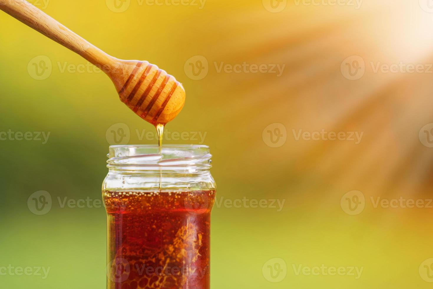 miele che gocciola dal mestolo di miele su sfondo naturale foto