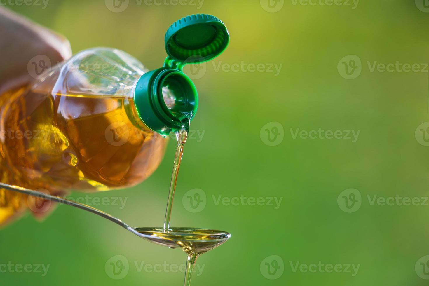 mano versando olio vegetale dalla bottiglia al cucchiaio foto