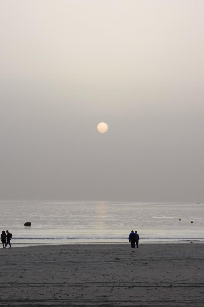 solitario spiaggia con persone passeggiando su il sabbia a il bordo di il mare onde foto