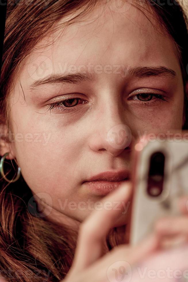 un' adolescenziale ragazza è pianto guardare a un' smartphone. un' adolescenziale ragazza è rovesciato. foto