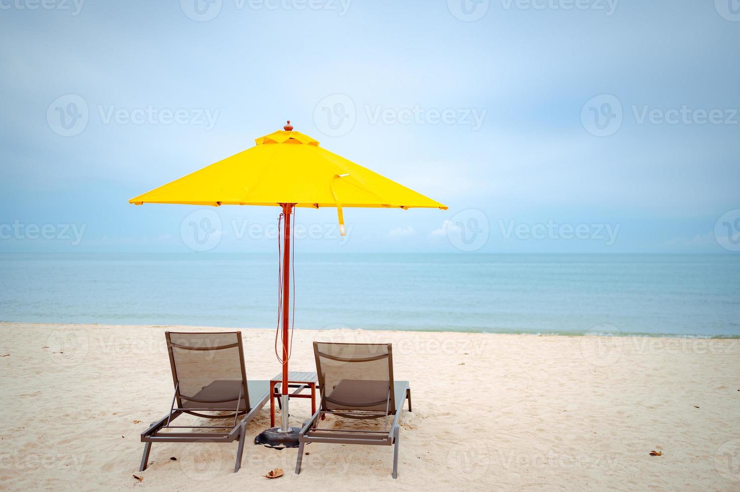 sedie a sdraio sotto un ombrellone giallo sulla spiaggia foto