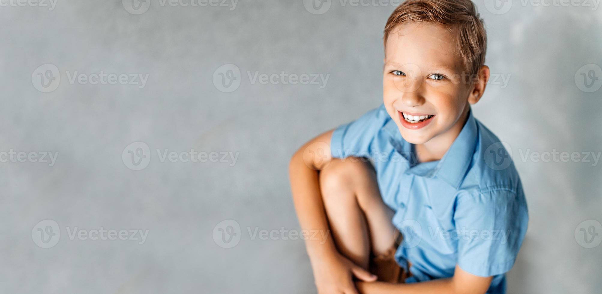 un' contento ragazzo nel un' blu camicia è seduta su un' sedia foto