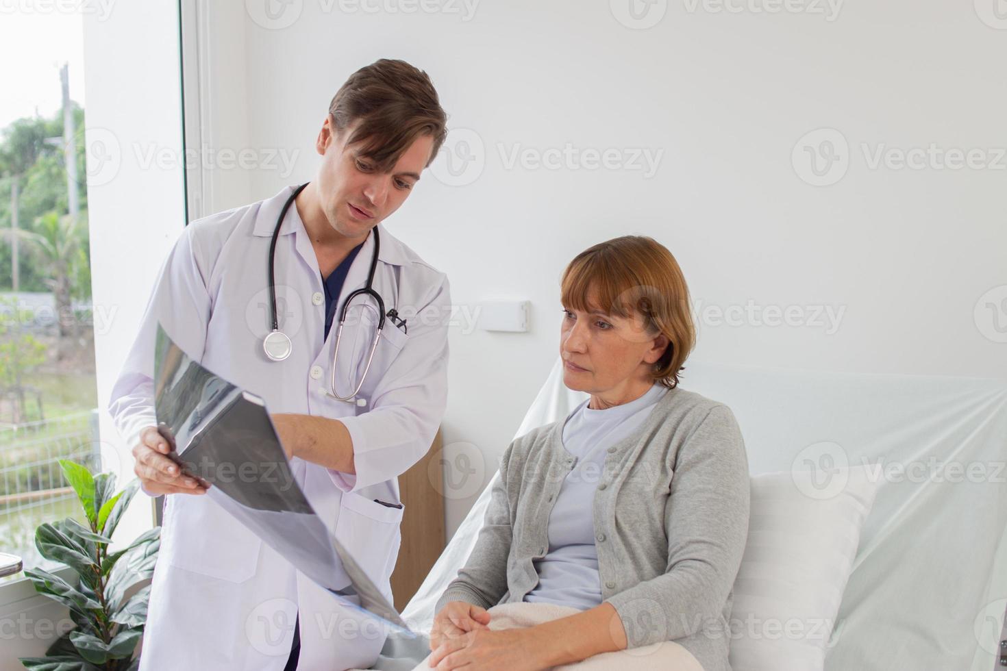 il medico è l'esame il paziente nel il Ospedale. caucasico medico indossare toga e ascoltando dispositivo mostrando raggi X film con un' femmina paziente a il ospedale foto