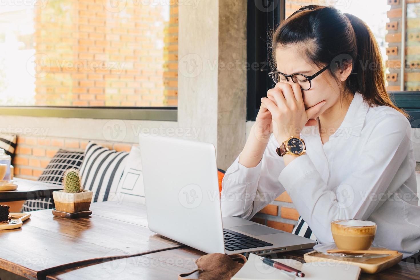 asiatico donna d'affari avendo mal di testa mentre Lavorando su sua il computer portatile nel ufficio. un' mal di testa è dolore o disagio nel il testa o viso la zona. foto