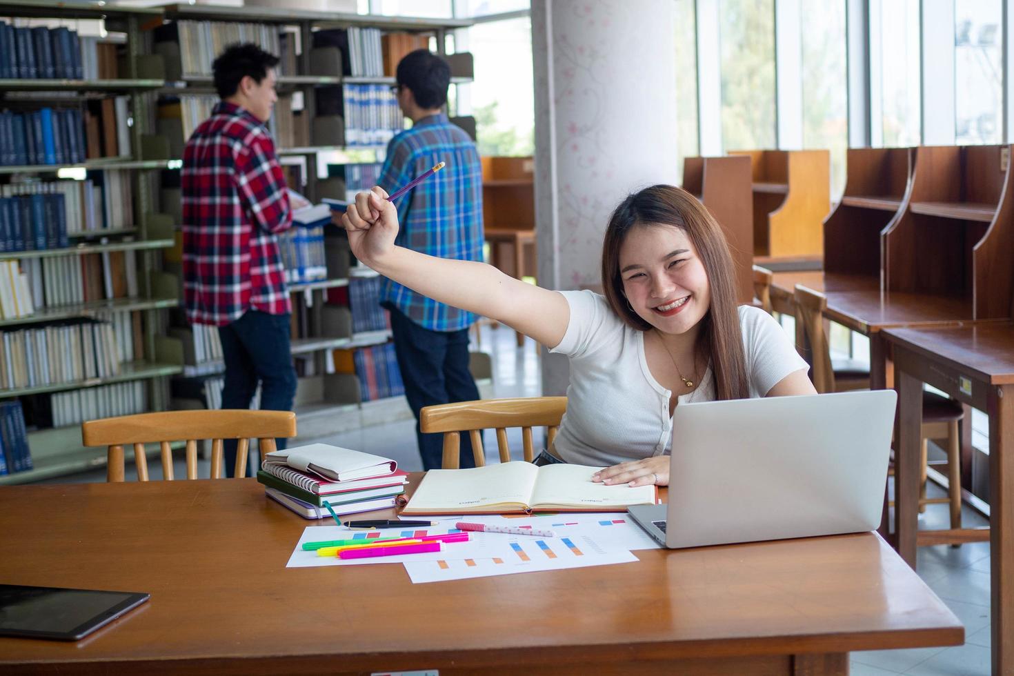 femmina studenti siamo stressato con lettura un' lotto di libri posto su il tavoli nel il biblioteca. per preparare per il esame foto