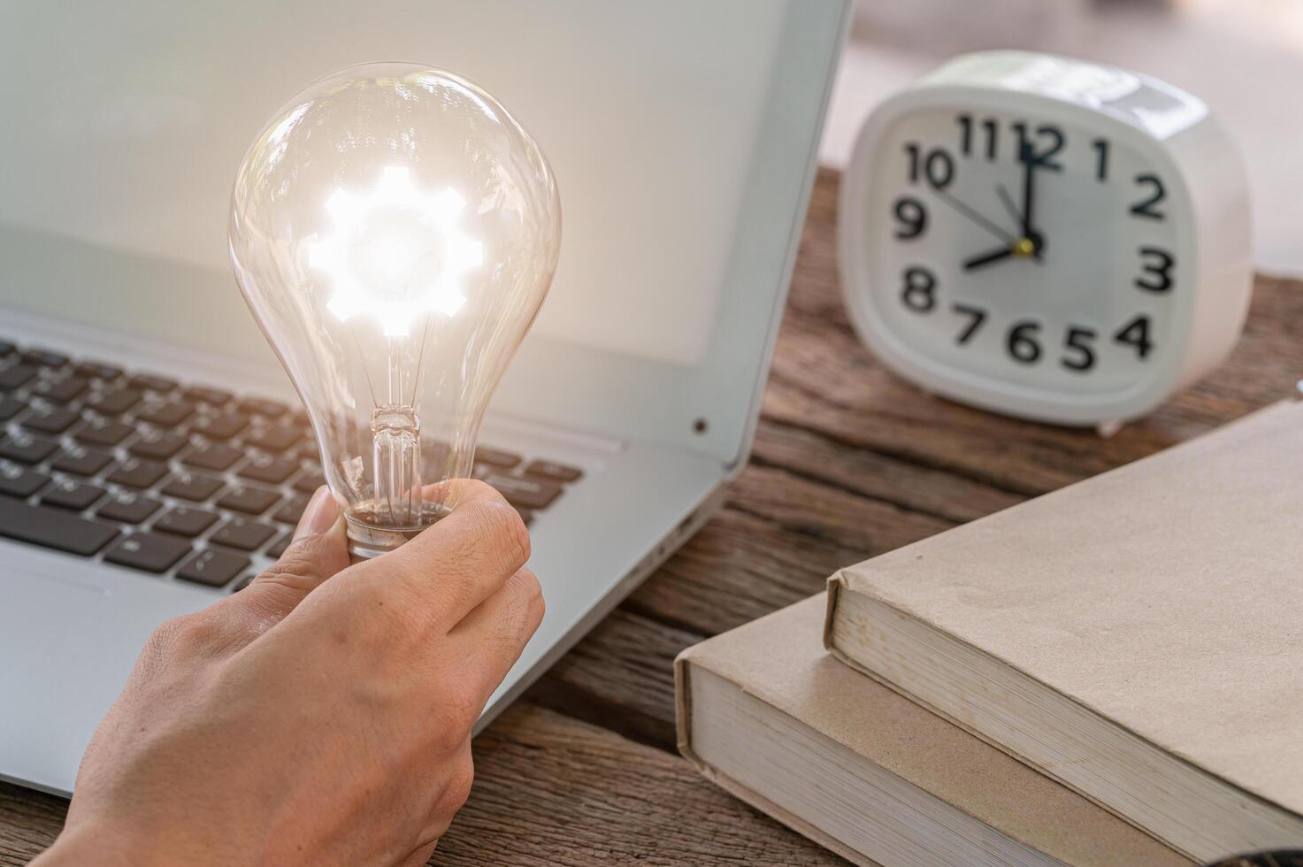 un uomo che tiene un simbolo dell'ingranaggio della lampadina mentre si utilizza un computer foto