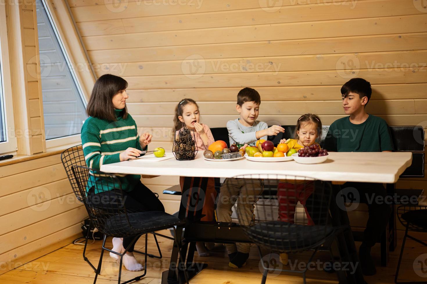 madre con quattro bambini mangiare frutta nel di legno nazione Casa su fine settimana. foto